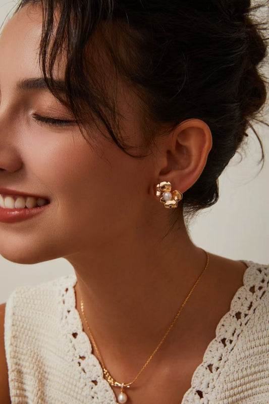 Boucles d’oreilles dorées en forme de fleur avec perle, portées avec collier