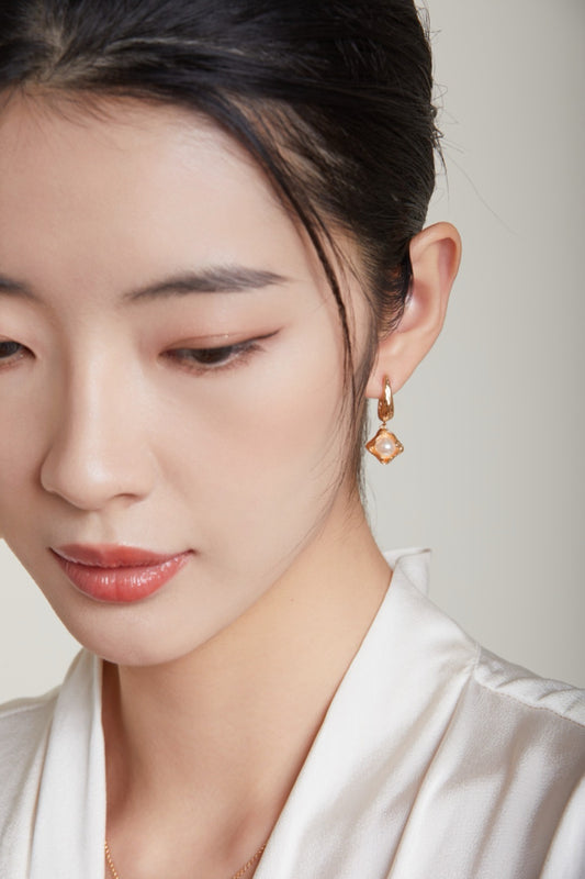 Boucles d’oreilles pendantes en perles naturelles et doré portées par un modèle femme