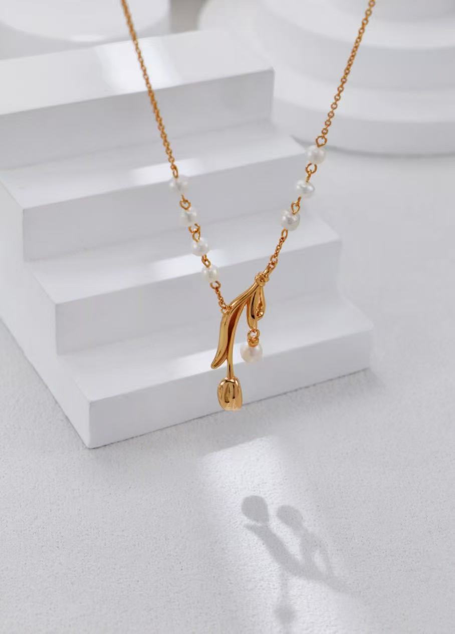 Collier doré avec pendentif floral et perles naturelles sur fond blanc en studio.