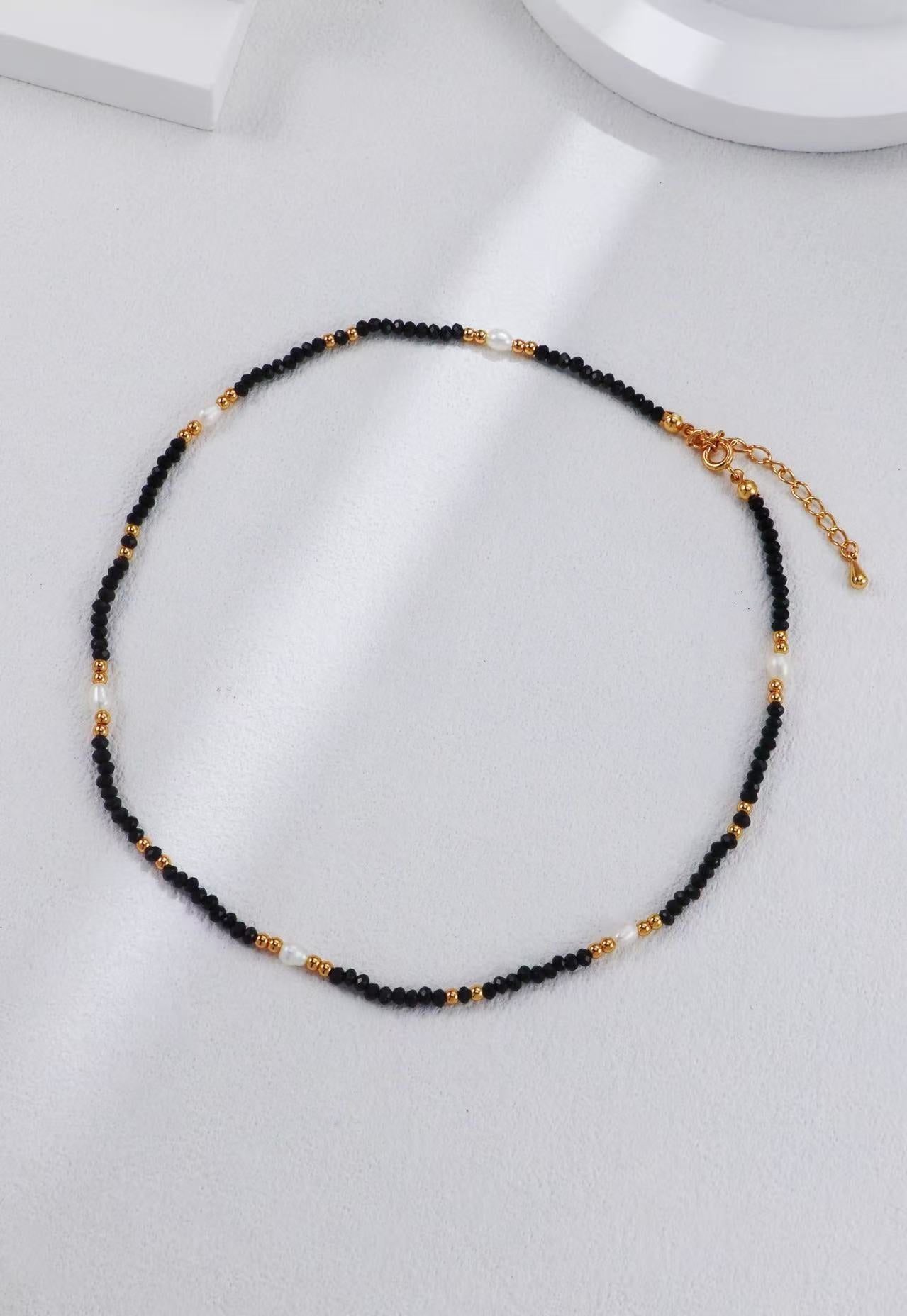 Collier Éclipse Dorée en perles noires et dorées avec fermoir mousqueton en argent S925, présenté à plat
