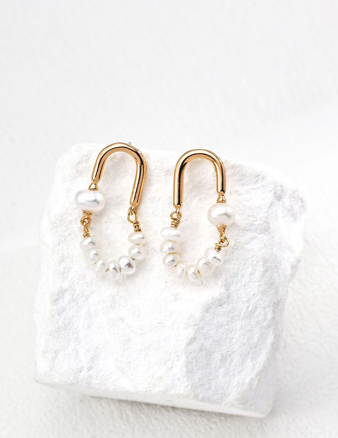 Boucles créoles dorées avec perles naturelles posées sur fond blanc