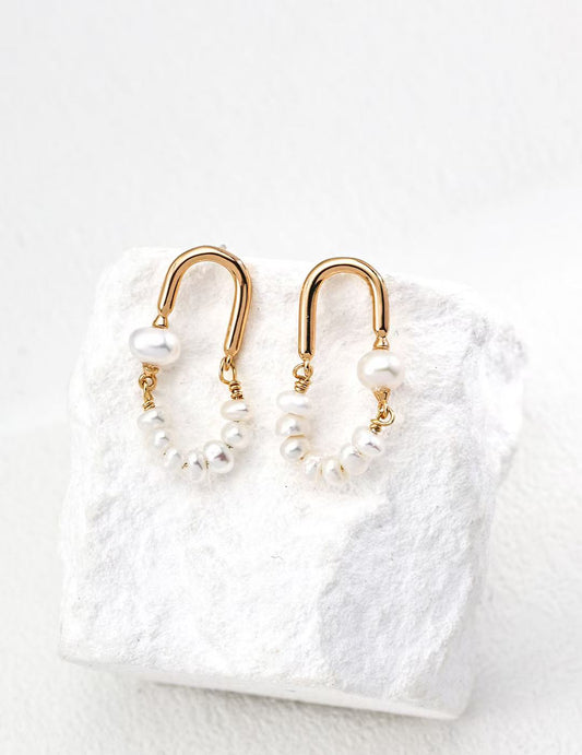 Boucles créoles dorées avec perles naturelles posées sur fond blanc