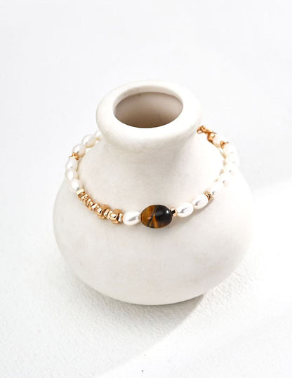 Bracelet œil de tigre MeiPerle posé sur un vase en céramique blanche – ambiance douce