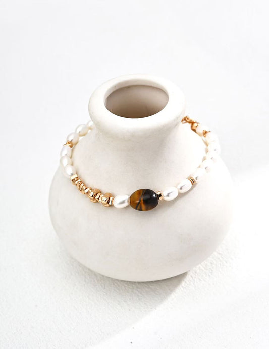 Bracelet œil de tigre MeiPerle posé sur un vase en céramique blanche – ambiance douce