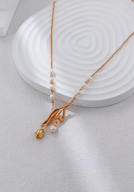 Collier doré avec pendentif floral et perles naturelles sur fond blanc en studio.