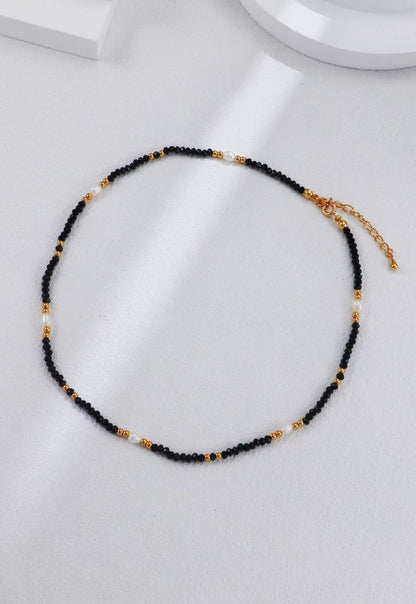 Collier Éclipse Dorée en perles noires et dorées avec fermoir mousqueton en argent S925, présenté à plat