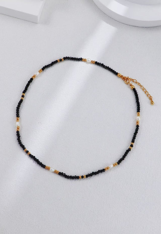 Collier Éclipse Dorée en perles noires et dorées avec fermoir mousqueton en argent S925, présenté à plat